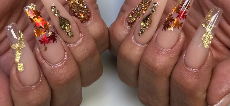 Autumn-themed nails with gold glitter, leaf designs, and jewel accents on a nude base. Perfect fall nail look created at NAB Nail Bar in Las Vegas.